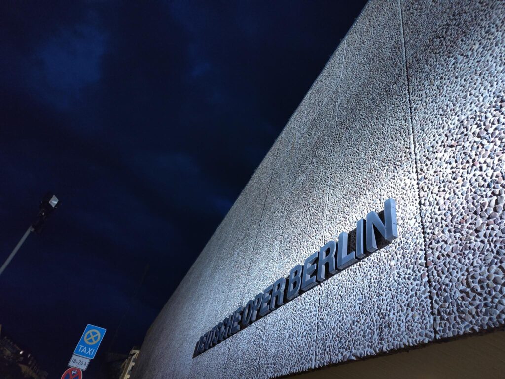Illuminated Deutsche Oper sign on the building facade at night in Berlin, capturing the city’s romantic ambiance.