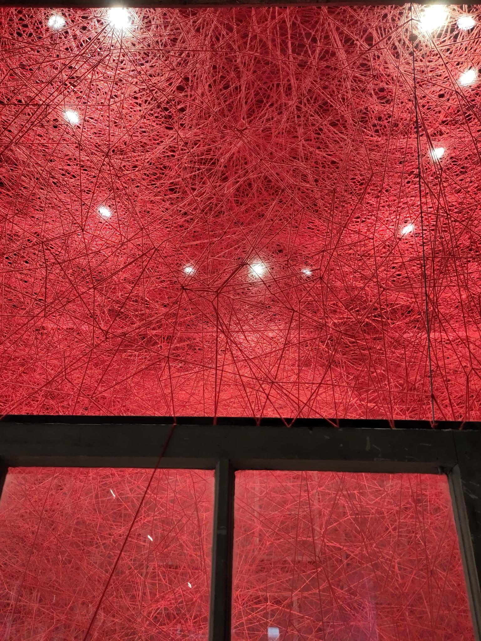 Lights shining through red threads at Königs Galerie exhibition in Berlin, showcasing sensory design and texture.