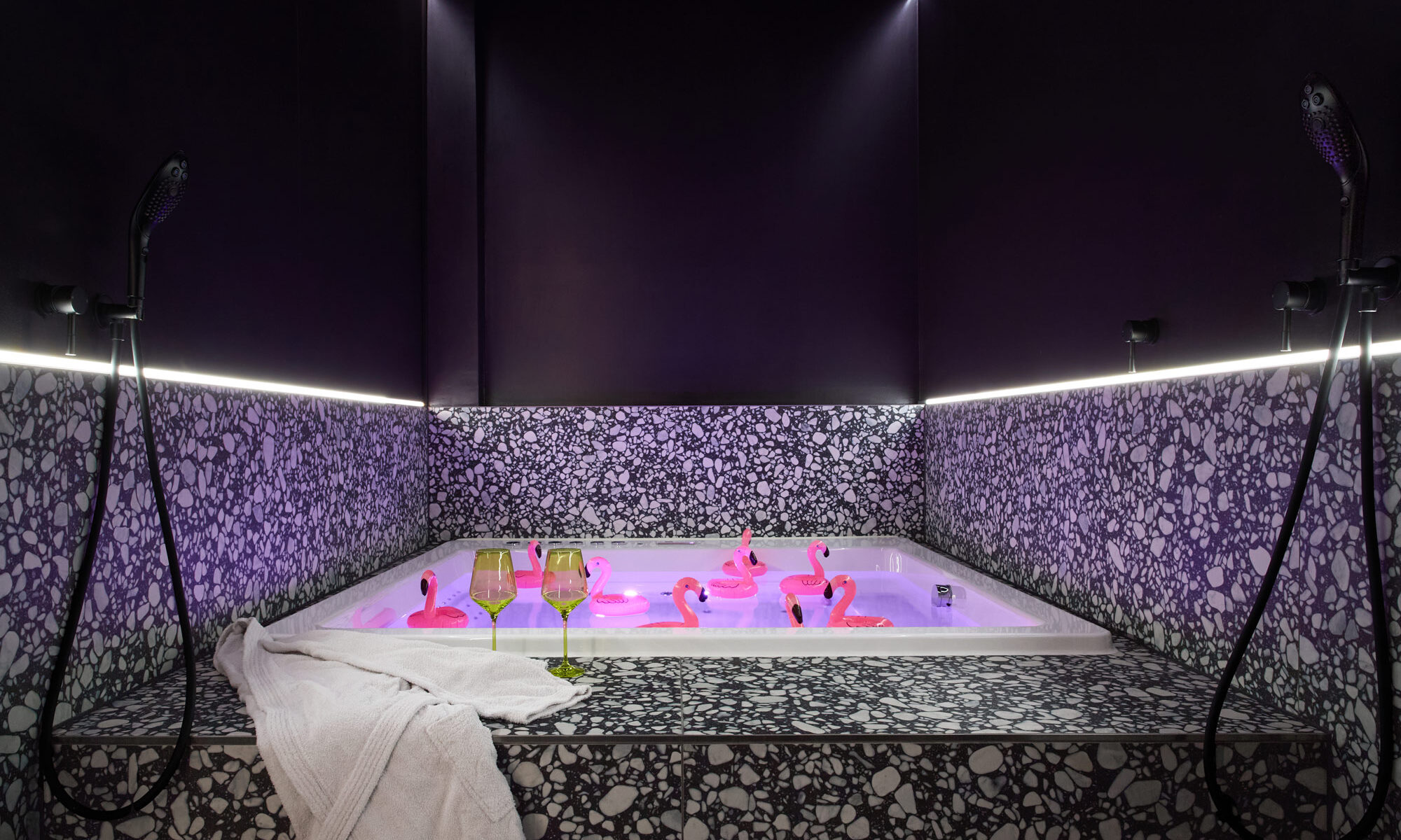 A playful view of the premium jacuzzi at The Circle Berlin private spa, decorated with 10 pink plastic flamingos, a luxury bathrobe, and elegant wine glasses.