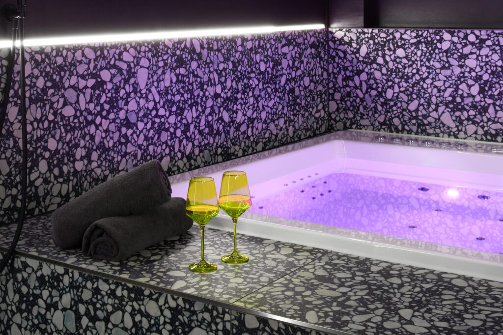 Zwei gelbe Weingläser auf beheizten Stufen, ein 1,80x1,80 cm Whirlpool mit lila Licht, Womanizer-Dusche & edles Terrazzo. Erlebt Luxus im The Circle Berlin privates Spa!