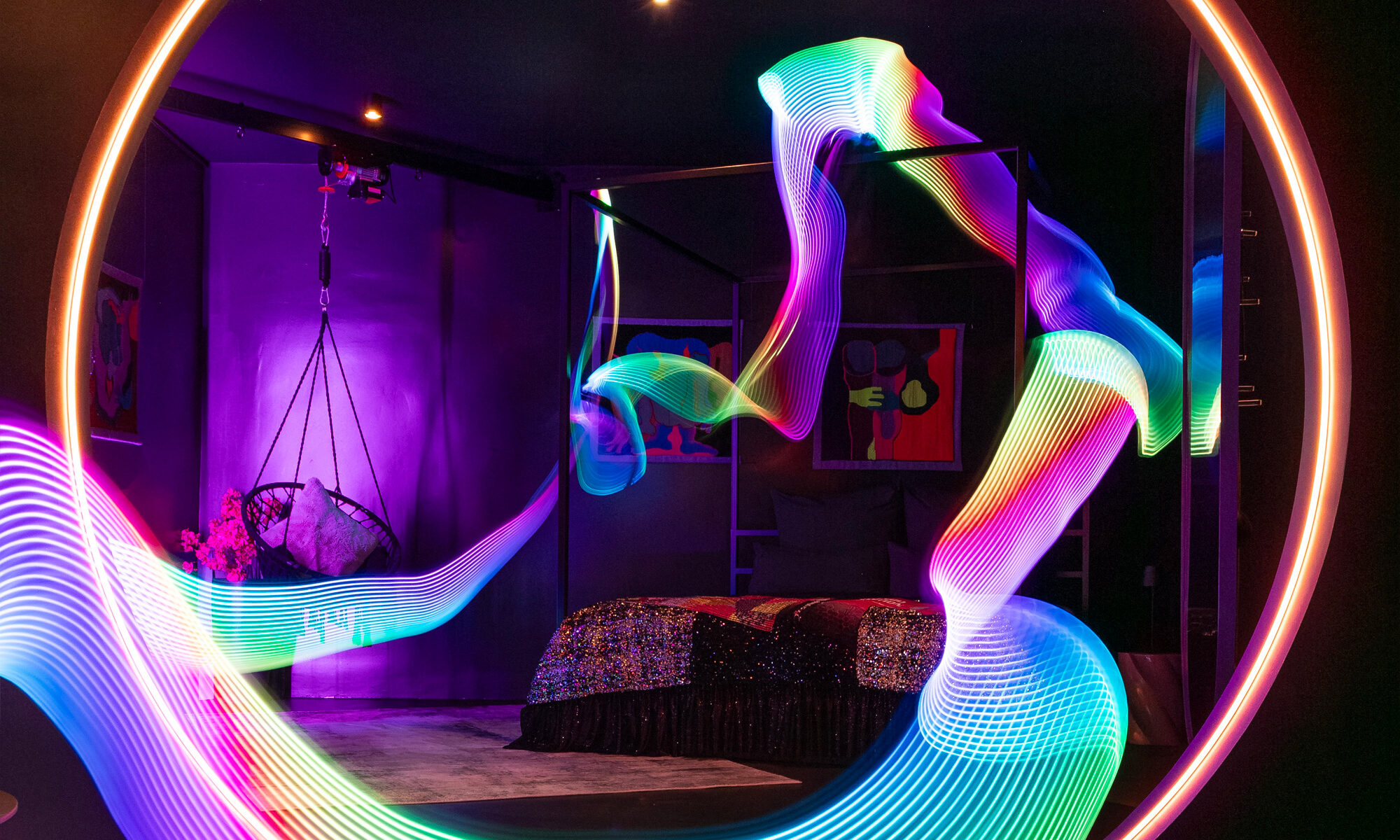 A view from the kitchen and lounge area looking into the bedroom suite at The Circle Berlin private spa, showcasing the custom-made kingsize 4-poster bed with a Tata Christiane sequined bedspread under colorful, whimsical lighting effects by Electric Skin.